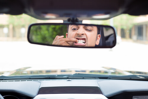 Man inspecting his dental bridge in car mirror, considering a replacement in the Philippines